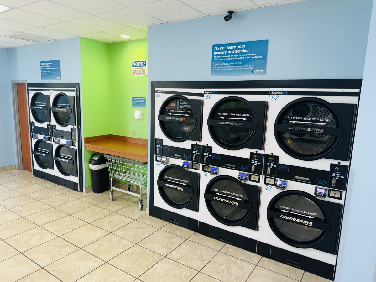 Dryers beside a folding table at Express Laundry Center, where drop-off orders are folded